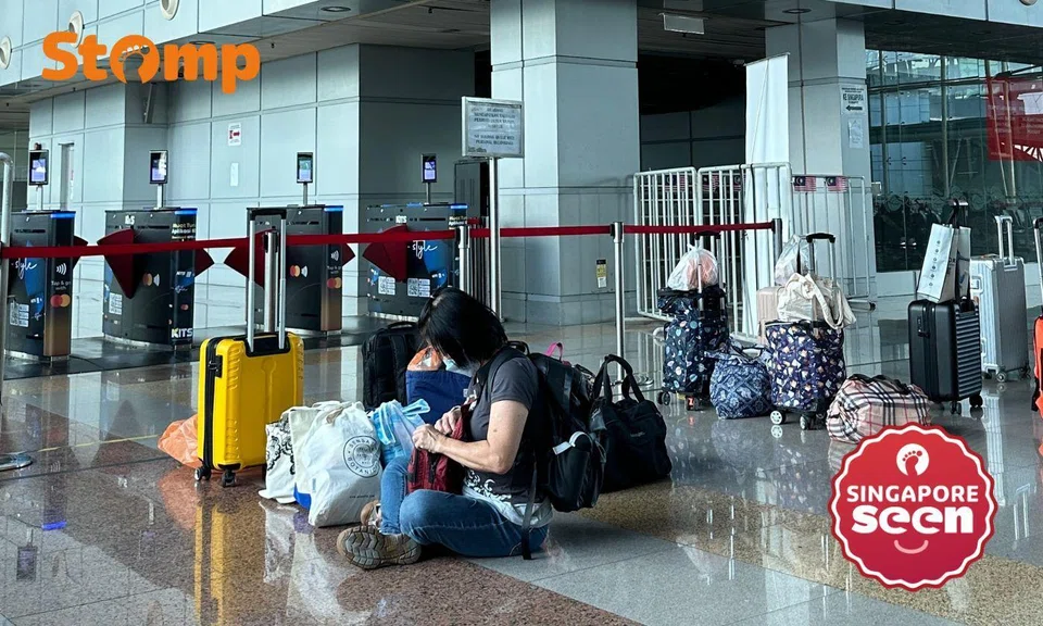 Travellers leave luggage unattended to reserve their spot in the queue, a woman sitting in the centre of the image attends to her own belongings