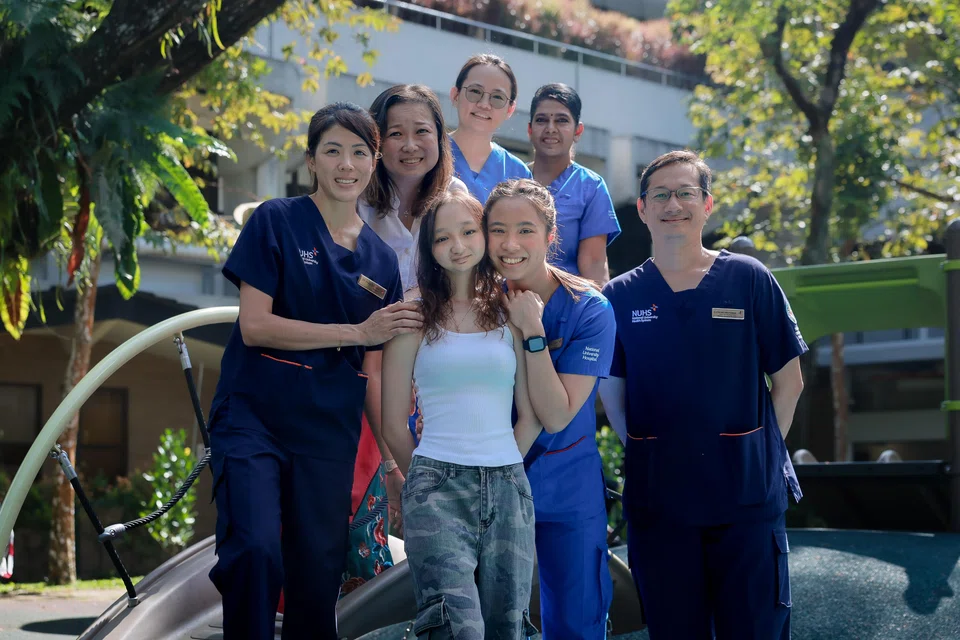 Sara Grace Kueh (centre, white top) and the team that has taken care of her since she was one. (Anti-clockwise from Sara) Ms Isabelle Joy Kueh, Adjunct Professor Mark Puhaindran, nurse manager Santha T Vengadasalam, staff nurse Lai Xiaoling, mother Esther Kueh and Dr Frances Yeap.