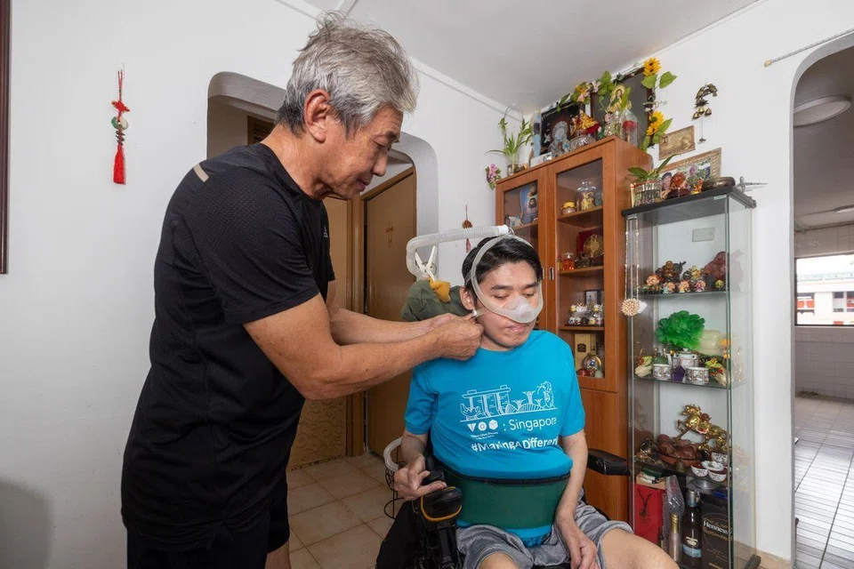 Mr Steven Eng helping to put on the oxygen mask strap of a ventilator to help Mr William Eng with his breathing.