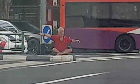 Why is this elderly man sitting on central road divider outside AMK Hub?