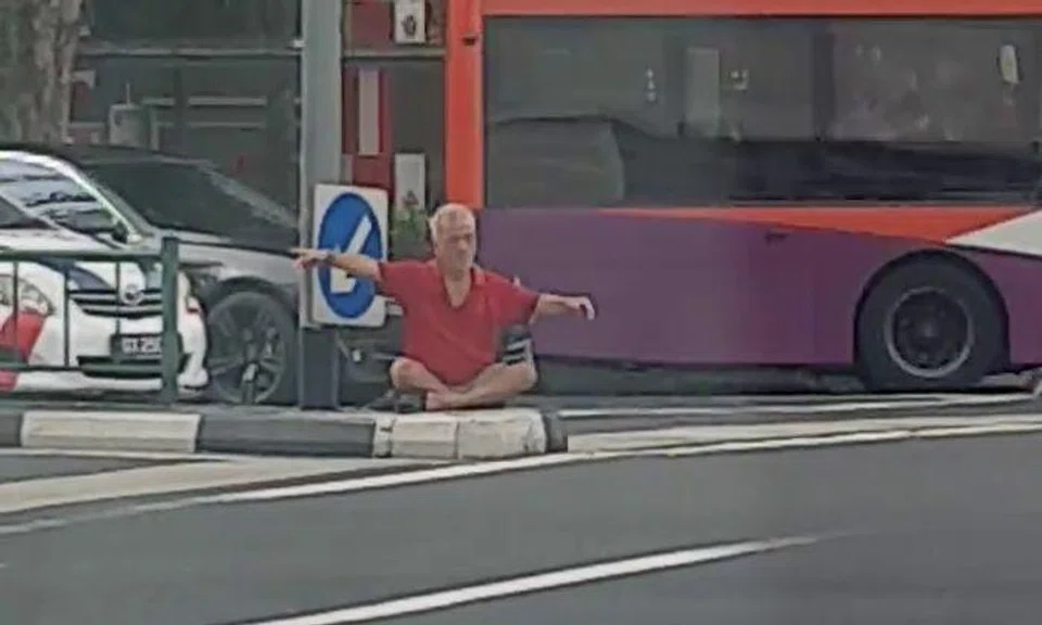 Why is this elderly man sitting on central road divider outside AMK Hub?