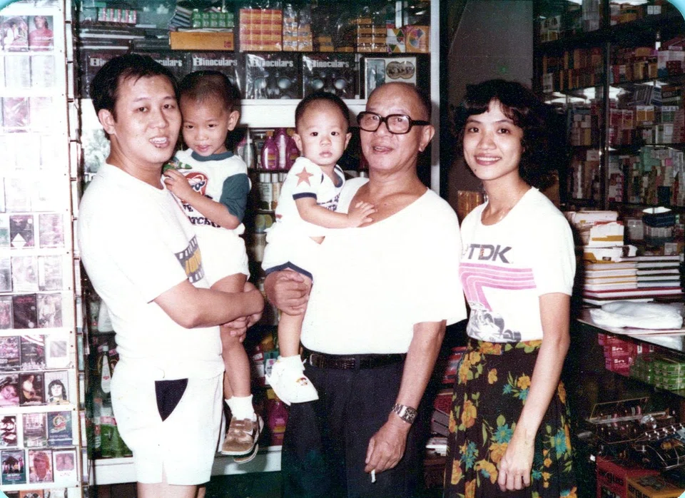 A family photo taken at Joo Ann Foh's original shop in Holland Avenue in the 1980s. A section of the shop carried photography-related products, while another section offered daily provisions. Seen here are business founder Ng Chin Wah (with glasses), second-generation owner Paul Ng and his wife Irene Mah, and the couple's young sons Kenneth Ng (left) and Adam Ng.
