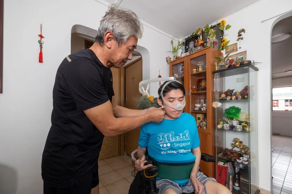 Mr Steven Eng helping to put on the oxygen mask strap of a ventilator to help Mr William Eng with his breathing.
