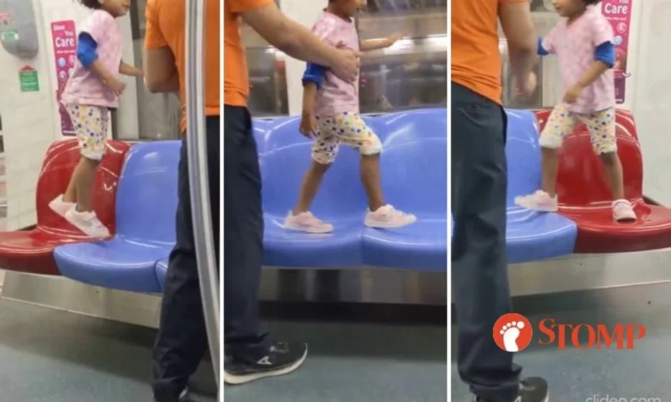 A man stood by as a little girl jumped and walked on the empty seats of an MRT train on the North-East Line.