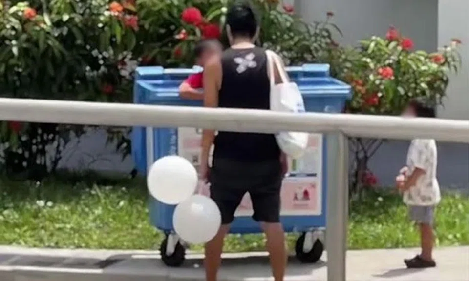 man scolds son in blue recycling bin