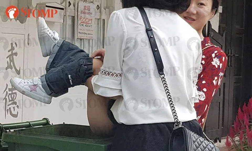 Adults help child to relieve herself in trash bin -- metres away from shopfront