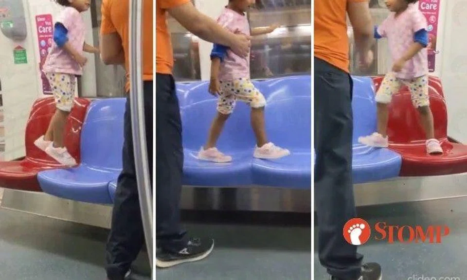 A man stood by as a little girl jumped and walked on the empty seats of an MRT train on the North-East Line.