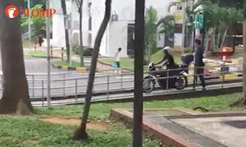 A motorcyclist can be seen riding down a walkway while a pedestrian had to lean on the railing to allow him to pass