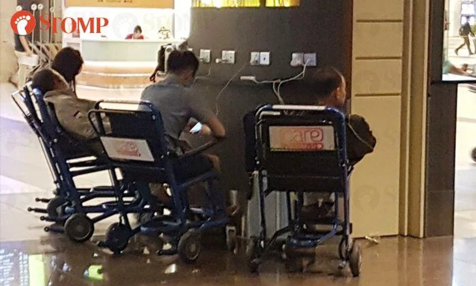 Visitors sit on wheelchairs to use charging ports at Changi Airport T2
