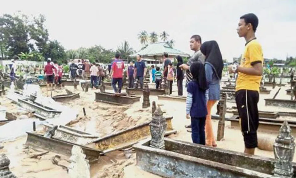 Nature’s fury: Residents looking at the graveyard in disbelief after swift currents wreaked havoc and four recently buried bodies were found floating nearby.  Photo: The Star/Asia News Network