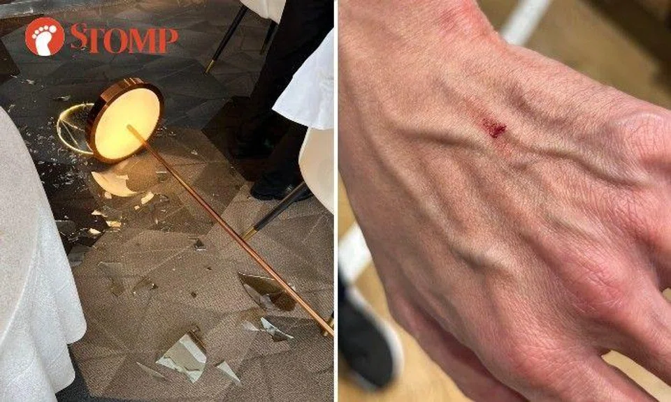 A floor lamp fell over and the glass lamp shade broke into pieces. As a result, a customer who was seated at a table next to this lamp suffered a minor cut.