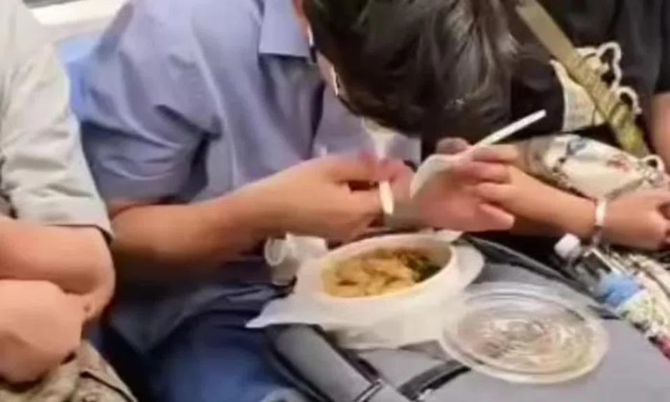 MRT passenger eats full meal with bowl on lap and utensils in hand, unfazed by stares