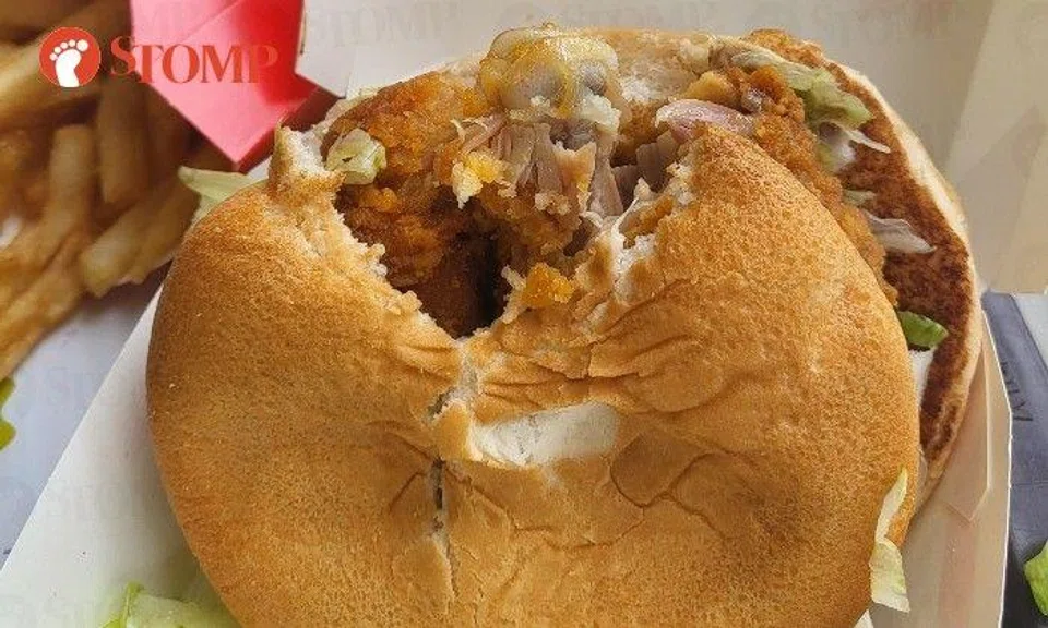 The photo shows a chicken burger with a bite taken out of it and a chicken bone sticking out of the patty between the buns.