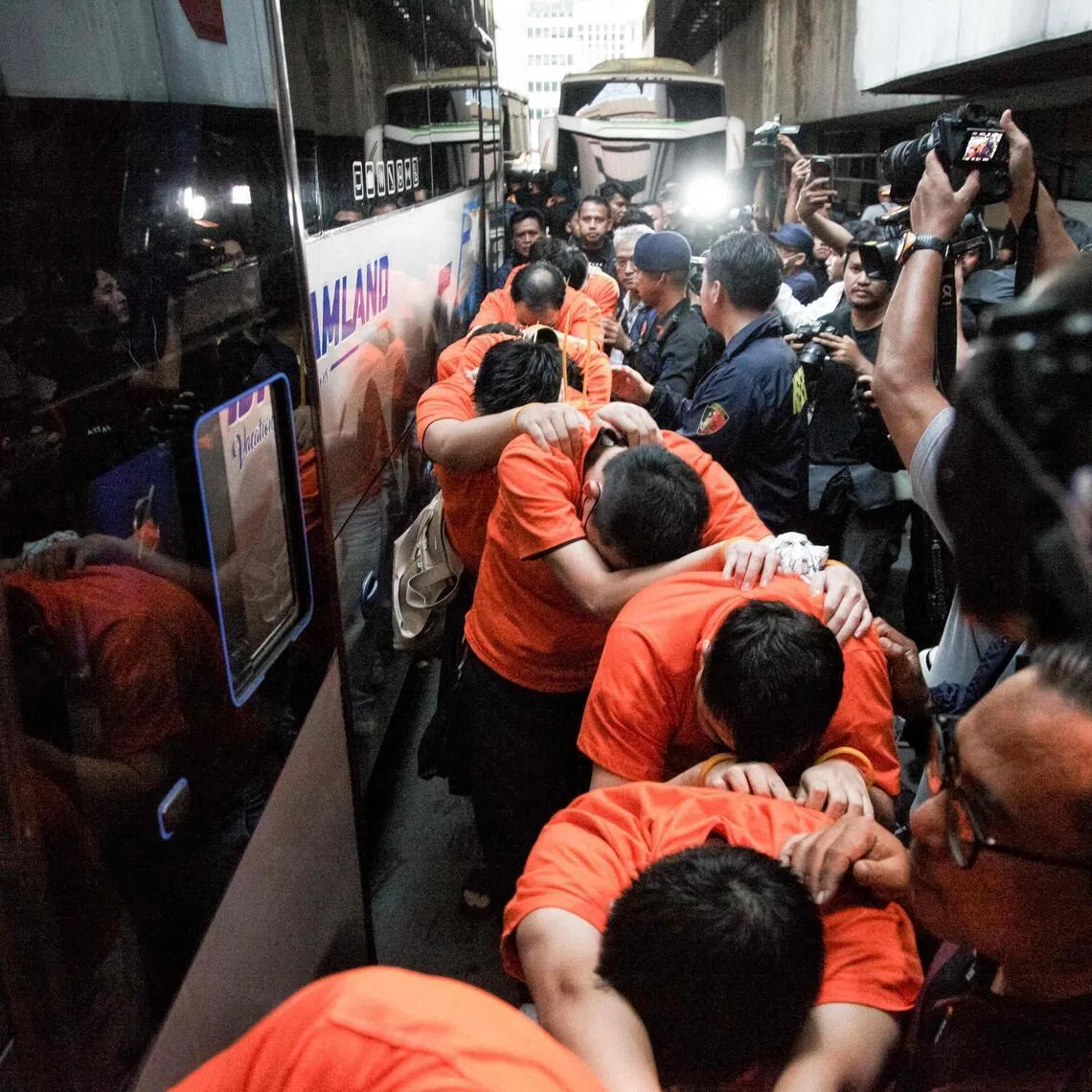 Suspected online gambling operators (in orange) walk towards buses for transfer after a police raid at the Hayam Wuruk Plaza office building in Jakarta on May 10.