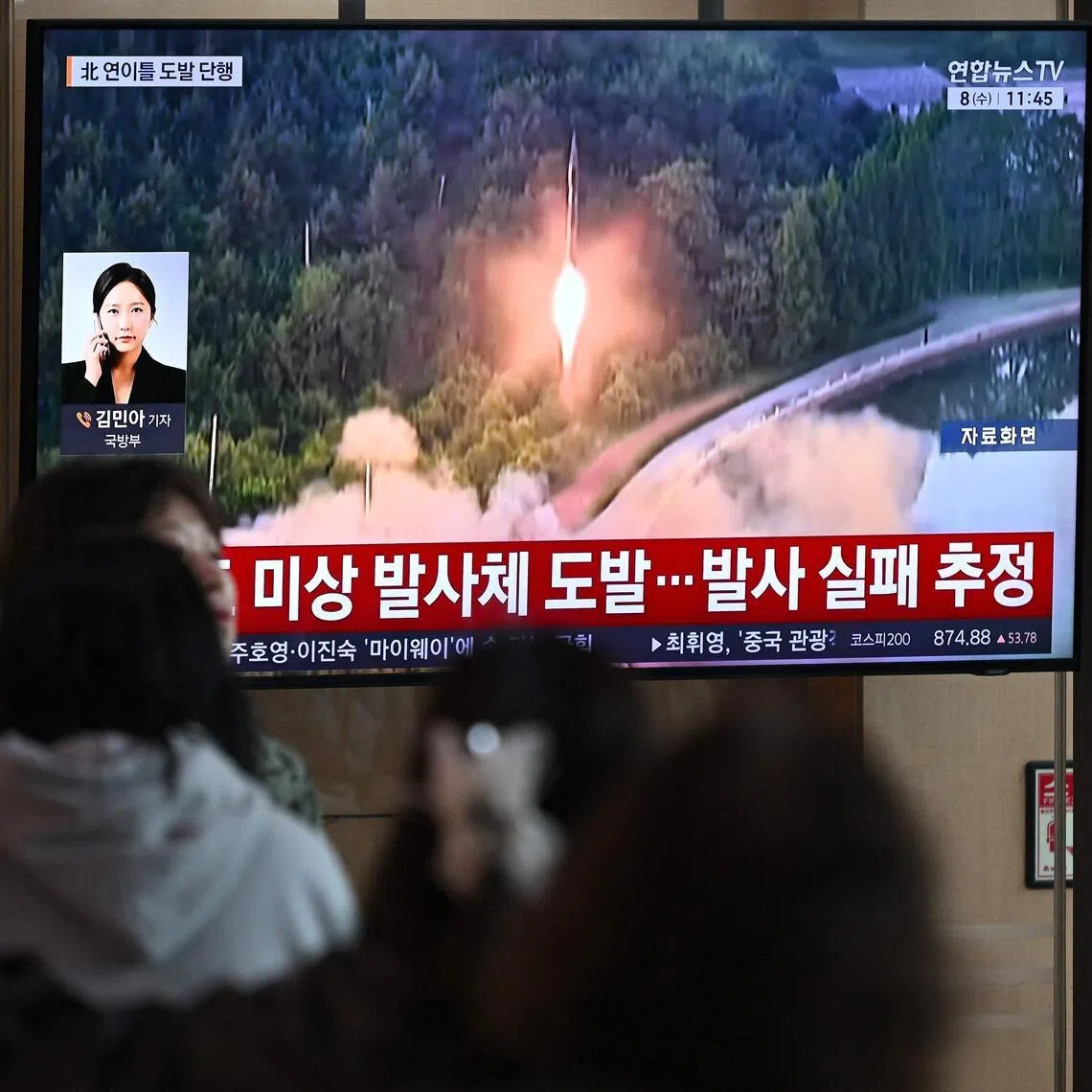 People watch a television screen showing a news broadcast with file footage of a North Korean missile test, at a train station in Seoul on April 8, 2026. 