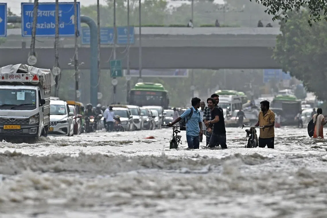 People wade through the flooded streets after Yamuna river over flowed due to monsoon rains in New Delhi on July 14, 2023. 