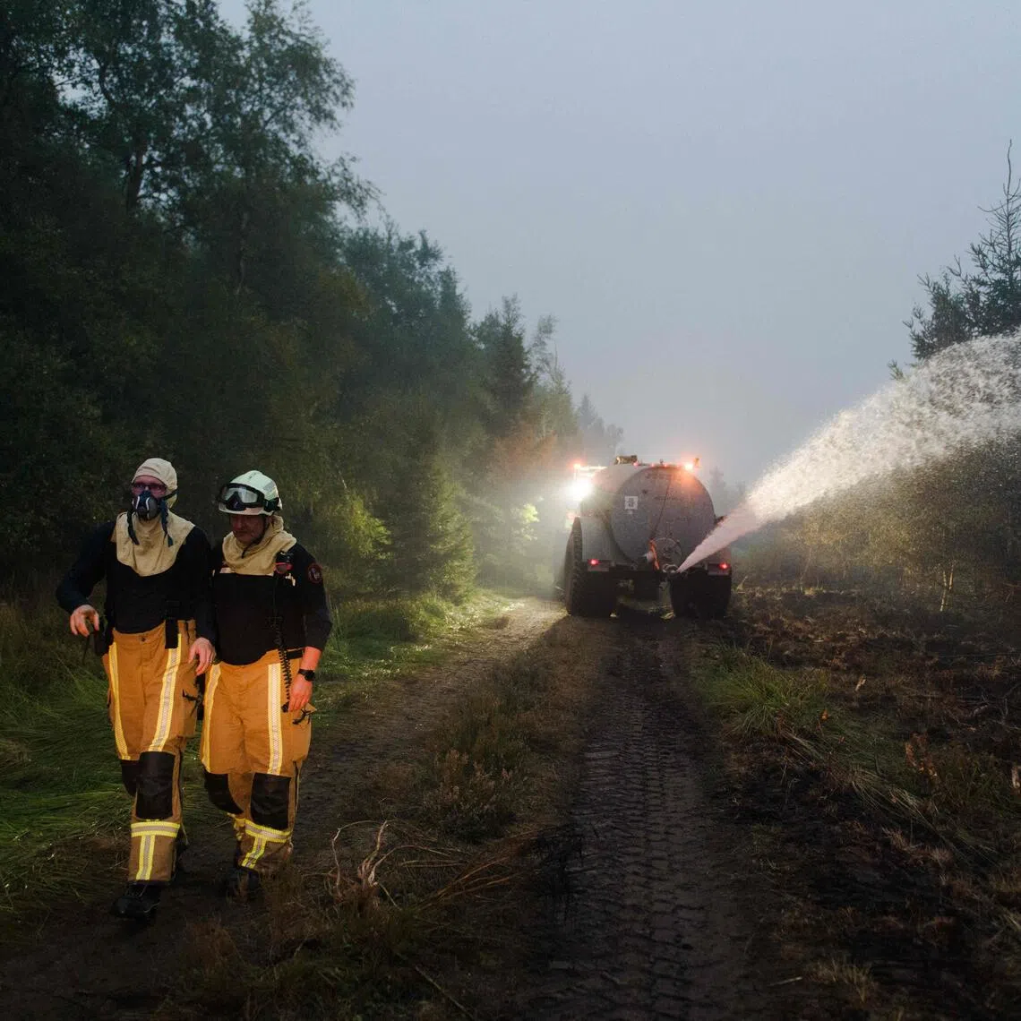 Firefighters walking along a road as farmers spray water with their tank to assist firefighters during operations against a wildfire at the Hautes Fagnes nature reserve near Sourbrodt, eastern Belgium, on Aug 17.
