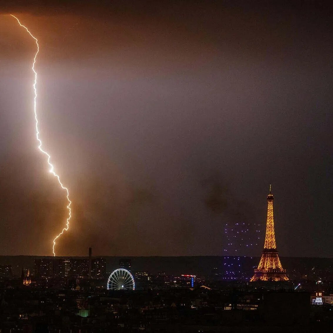 TOPSHOT - A ligthing strikes as fireworks light up around the Eiffel Tower during a choreographed firework and drone show to celebrate Bastille Day, in Paris, on July 13, 2026, on the eve of the annual Bastille Day Parade in the French capital. (Photo by DIMITAR DILKOFF / AFP)