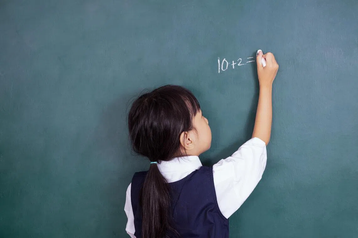 Asian Chinese little girl writing on blackboard in the classroom.
