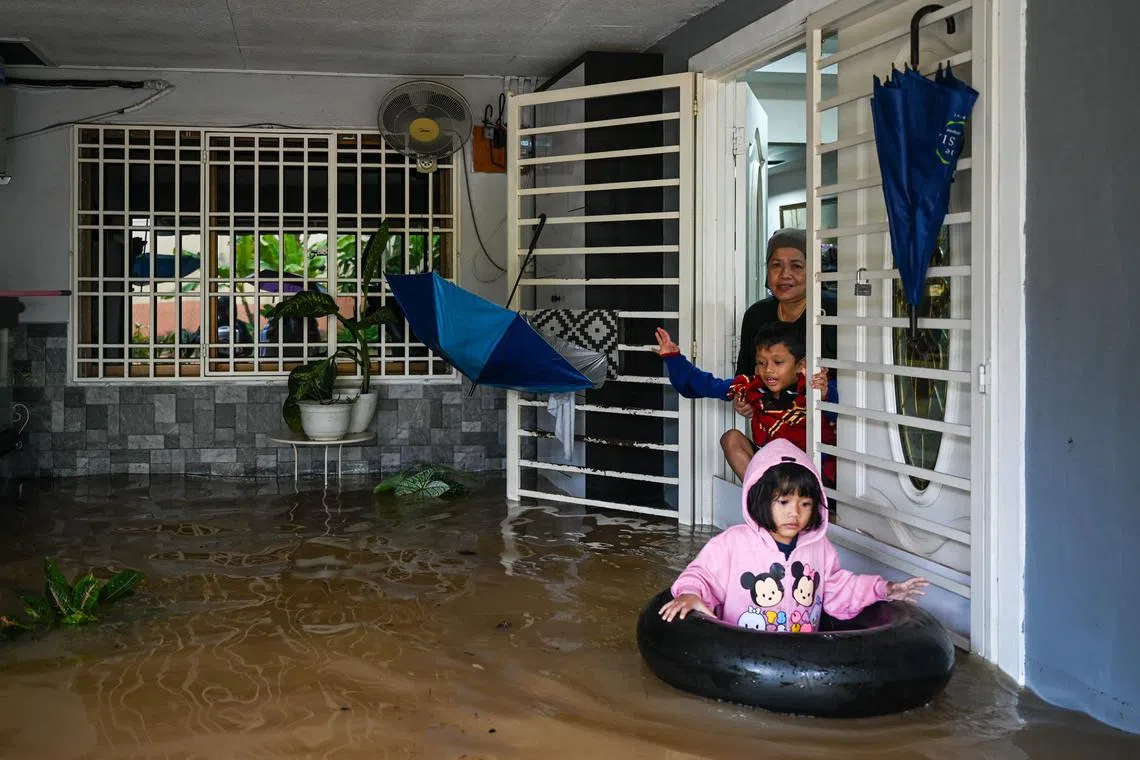 TOPSHOT - A woman and her children prepare to evacuate their home in a flooded area in Yong Peng, Malaysia's Johor state on March 4, 2023. (Photo by Mohd RASFAN / AFP)