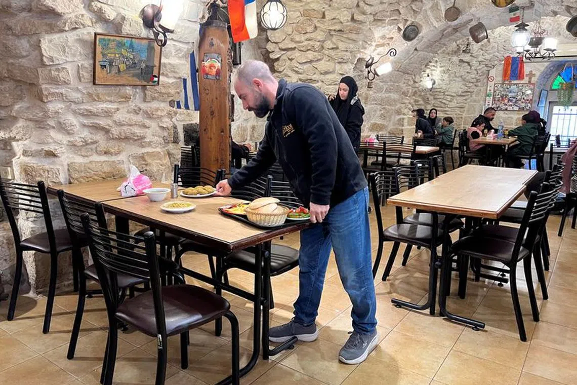 Fourth generation co-owner of Restaurant Afteem, Ala'a Salameh, 42, places food on a table inside the restaurant in Bethlehem, in the Israeli occupied West Bank, December 9, 2023. REUTERS/ Lucy Marks