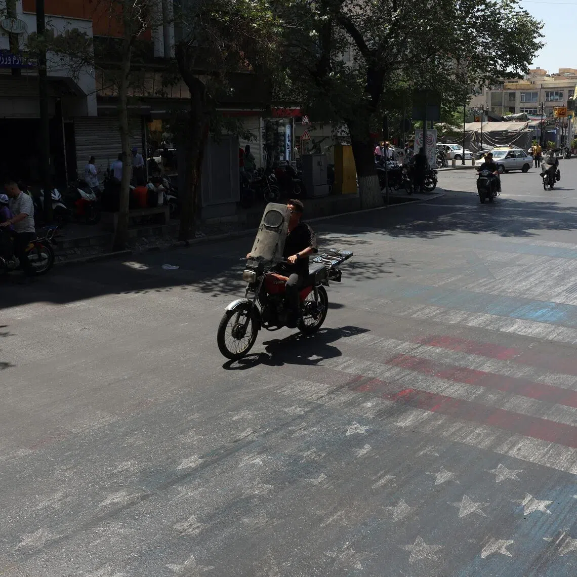 Iranians drive over a painting depicting the US flag in a street in Tehran, Iran, on June 10.