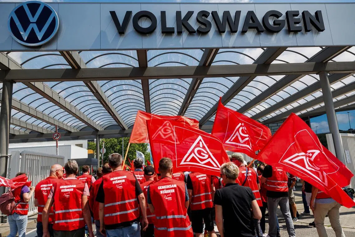 (FILES) Employees of German car maker Volkswagen (VW) carry flags of German trade union IG Metall as they take part in a rally to protest against restructuring and mass job cut plans at the VW plant in Zwickau, eastern Germany on July 9, 2026. Volkswagen's boss told employees on July 13, 2026 a further 50,000 jobs could go at the struggling auto giant, according to an internal memo seen by AFP, confirming reports the group is targeting 100,000 cuts worldwide. (Photo by Jens SCHLÜTER / AFP)