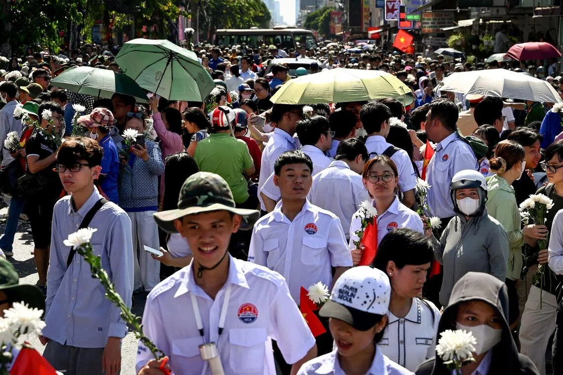 People holding white flowers gather as buses carrying caskets containing the remains of fallen soldiers pass by in Ho Chi Minh City on Oct 14.