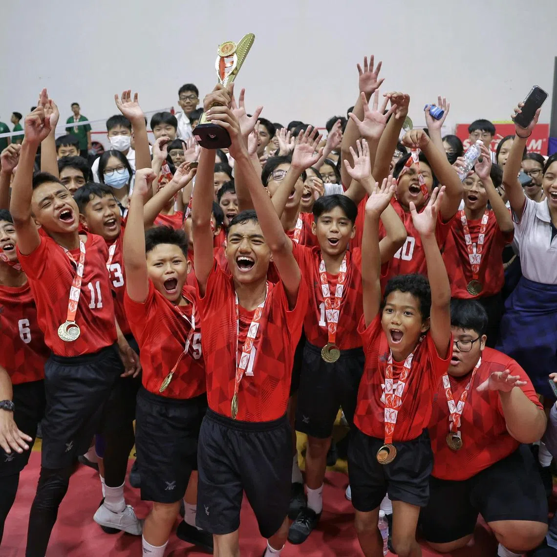 Marsiling Secondary School's Nick Daniel Maliqi Abdullah holding the trophy aloft as his team and supporters celebrating their win in the National School Games C Division boys sepak takraw final against Northlight School at Heartbeat@Bedok on Aug 12, 2024.