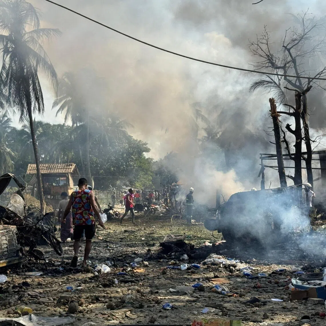 People walking through smoke and smouldering debris following an airstrike on a market and adjacent bridge in Kyauktaw, in Myanmar’s western Rakhine state on Sept 28.