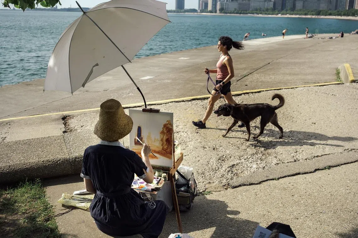 A painter paints under an umbrella from the Lake Front Trail, bordering Lake Michigan on June 21, 2025. Nearly a third of the U.S. population woke up to sweltering temperatures on Saturday as the first heat wave of the summer broke over the Midwest and Central Plains. 