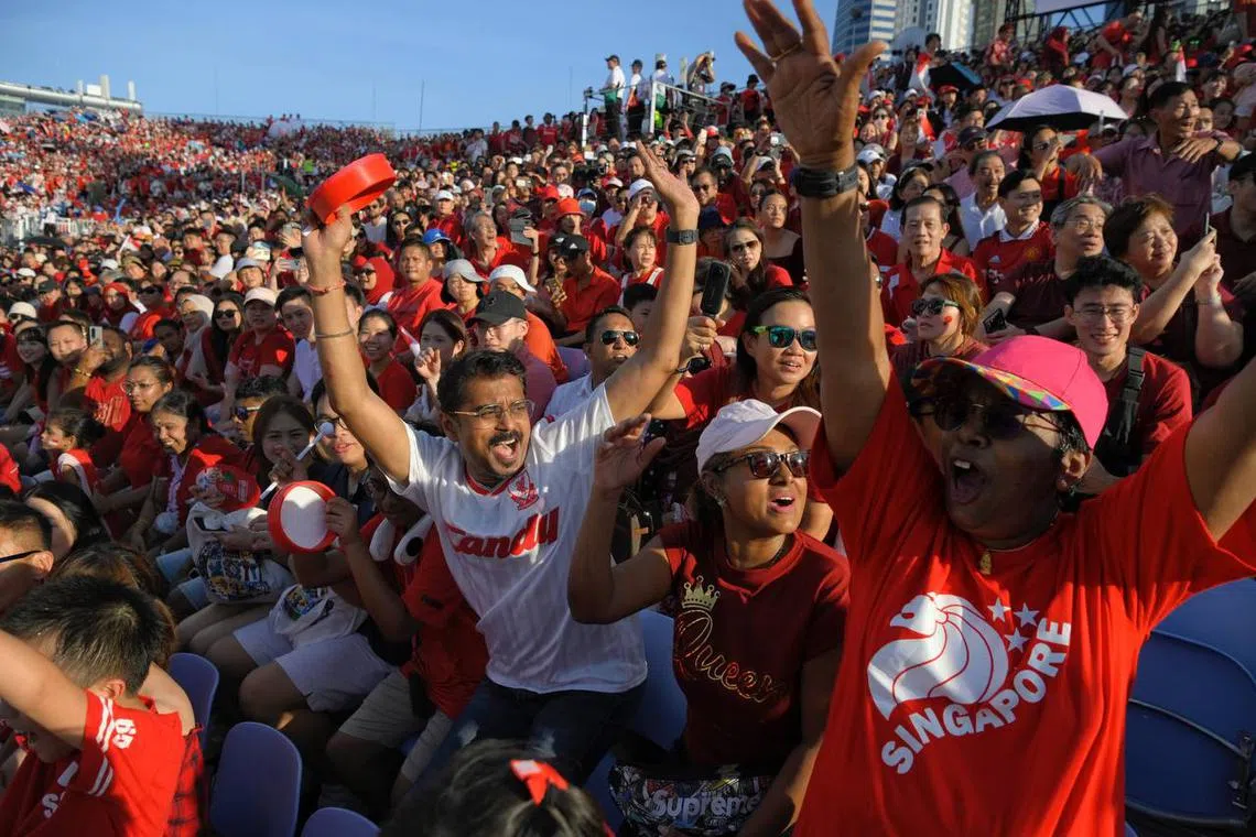 From centre left, Sivasangaran, 50, his friend Sheela Tanabalan, 37, and her mother Suseela Palanianandan, 67, seen doing the wave during the National Day Parade at the Padang on Aug 9, 2023. ST PHOTO: MARK CHEONG
