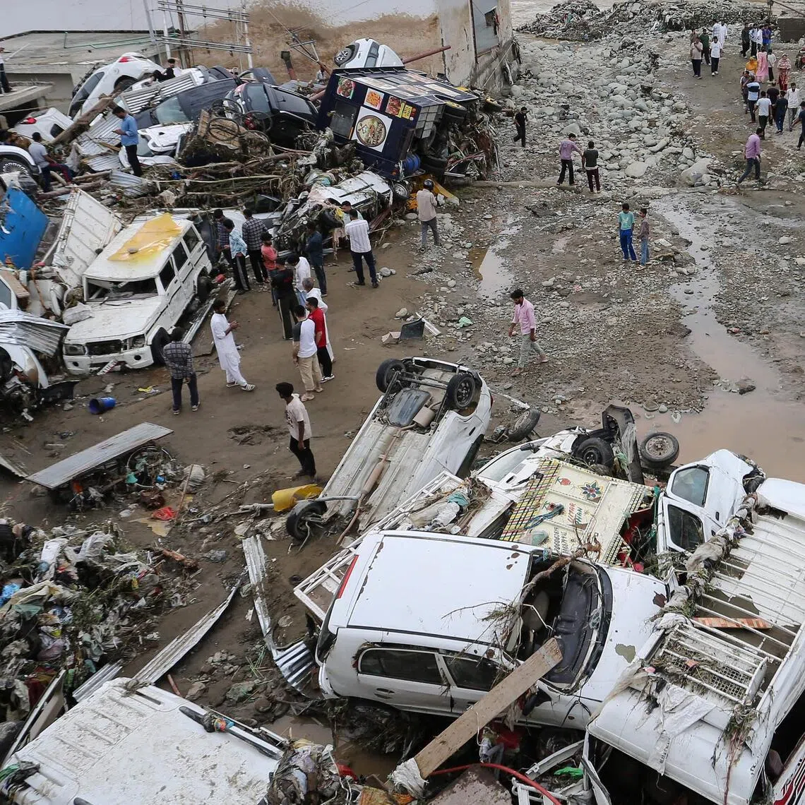 Residents look at damaged vehicles after flash flood and landslide triggered by heavy rains wreaked havoc at Rajouri district in India’s Jammu region on July 19.