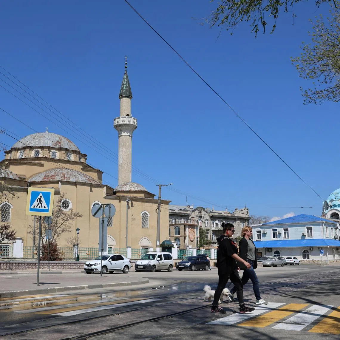 People cross the street near the Juma-Jami Mosque and the Saint Nicholas cathedral in Yevpatoriya, Crimea April 24, 2025. REUTERS/Alexey Pavlishak