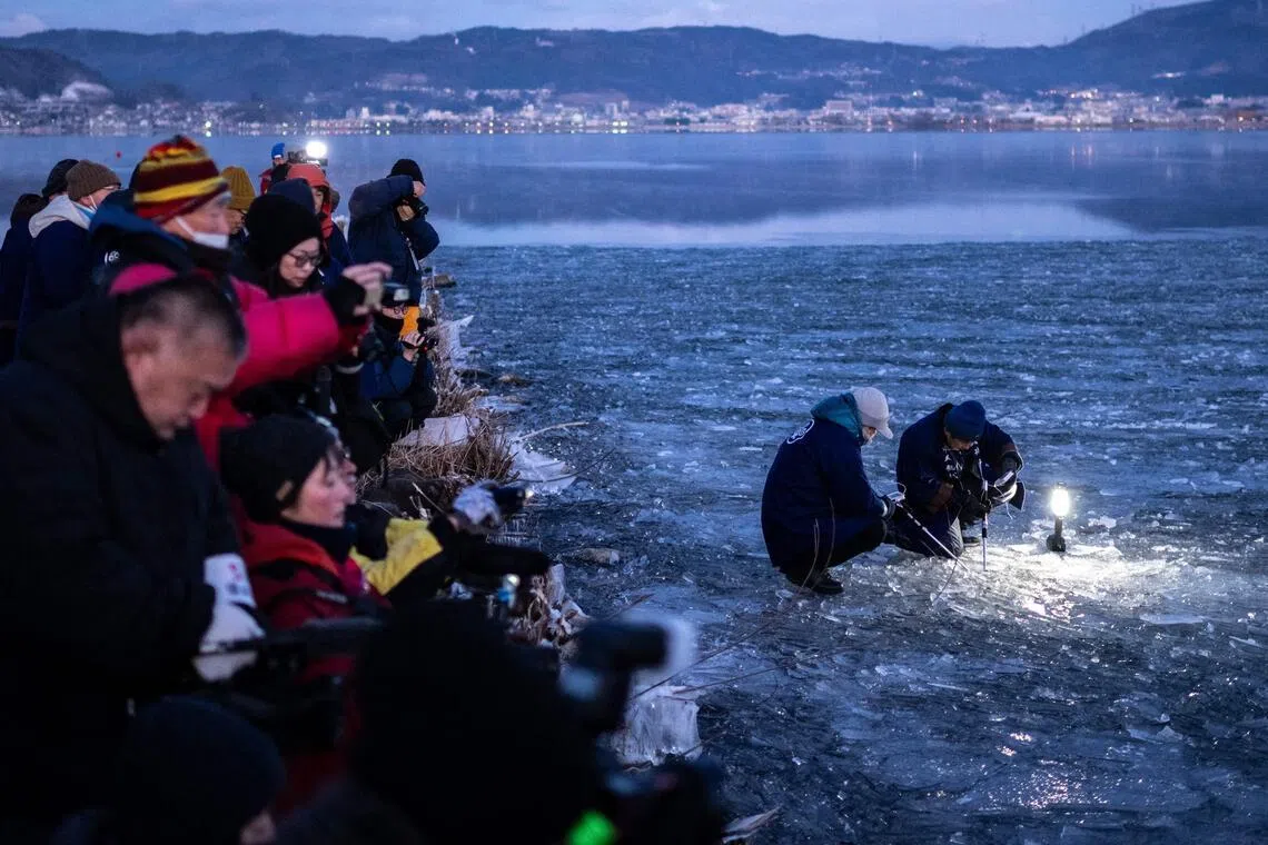 This picture taken early on January 29, 2026 shows members of the media filming the parishioners of Yatsurugi Shrine (R) measuring the ice of Lake Suwa of Nagano Prefecture. The Japanese priest and his parishioners gathered before dawn, hoping that climate change had not robbed them of the chance to experience an increasingly rare communion with the sacred. (Photo by Philip FONG / AFP) / To go with 'JAPAN-CLIMATE-RELIGION-NATURE-ENVIRONMENT-SCIENCE,REPORTAGE' by Harumi OZAWA