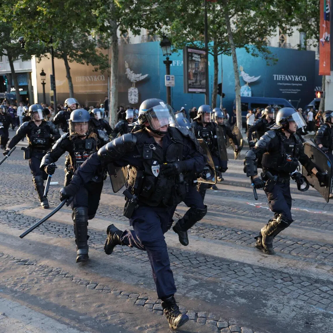 Police officers run to disperse PSG supporters on the Champs-Elysees Avenue during the Champions League final.
