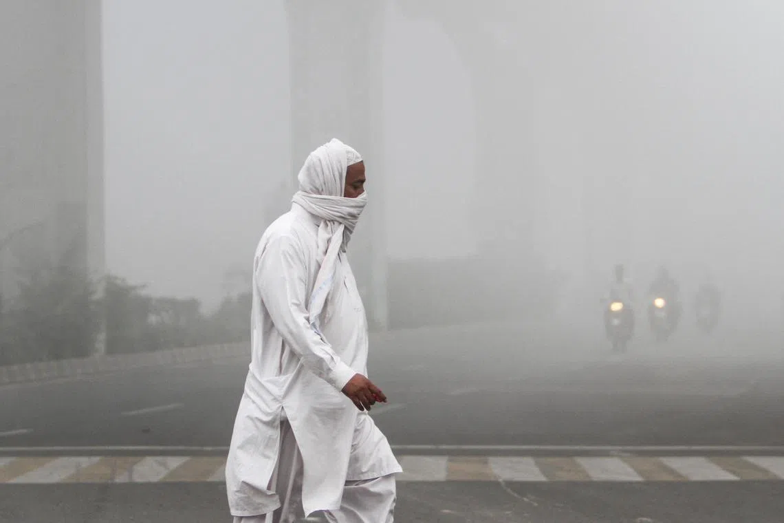 A man covers his face with a scarf to avoid smog as he walks along a road in Multan, Pakistan.