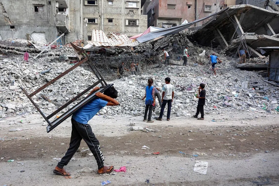 TOPSHOT - A boy walks carrying a table on his back past salvage workers scrapping the rubble of a building that was destroyed during Israel's war against Hamas in Gaza, to use the recycled remains in the future, in Gaza City on August 16, 2026. The Palestinian Islamist group Hamas had said on August 15 that it asked the US-backed Board of Peace to "compel" Israel to implement its obligations under the first phase of the US-brokered ceasefire plan in Gaza and to approve the roadmap for its second phase, after its leader met with the US president's envoy Jared Kushner in Egypt. (Photo by Omar AL-QATTAA / AFP)