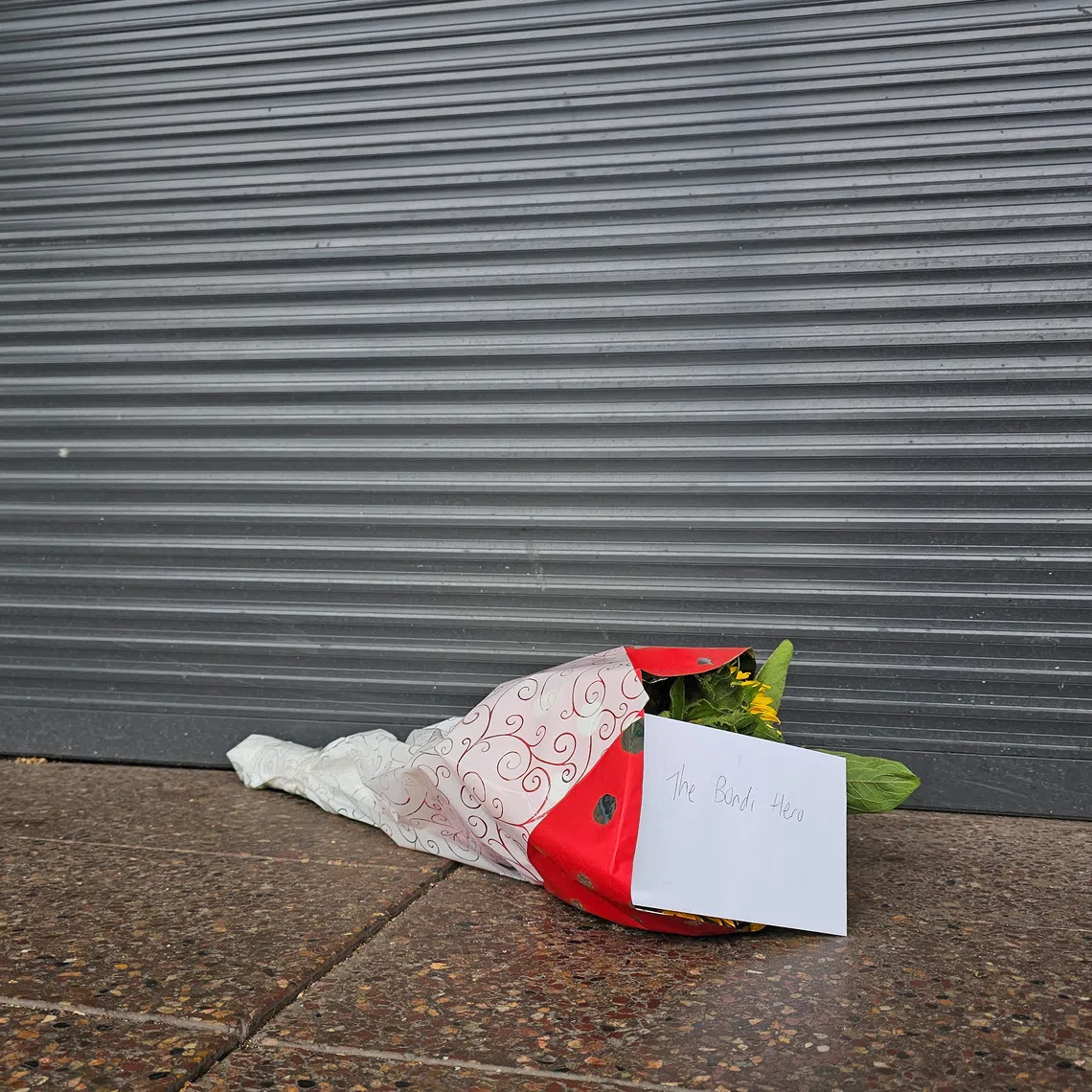 Flowers with a note that read \"The Bondi Hero\" are left outside tobacco shop owned by Ahmed al Ahmed, the bystander who is hailed as the \"Bondi hero\" after he charged at one of the gunmen and seized his rifle during the deadly shooting at Bondi Beach, in Sydney, Australia, December 16, 2025. Reuters/Cordelia Hsu