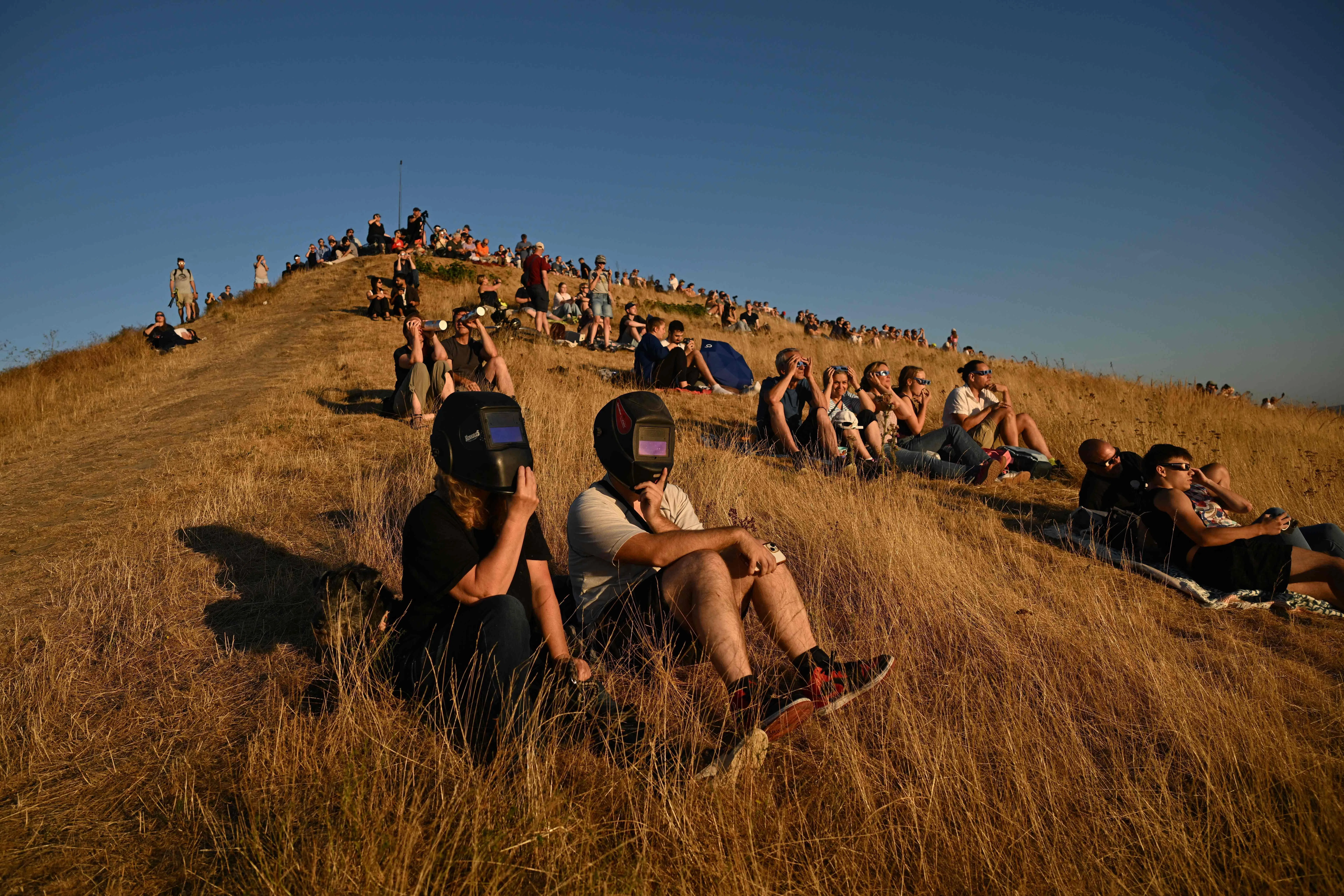 TOPSHOT - People look through welding shields during the solar partial eclipse in the landscape park Halde Hoheward in Herten, western Germany, on August 12, 2026. Millions of people turn their gaze towards the heavens on August 12, 2026 to witness one of nature's greatest spectacles -- a rare total solar eclipse -- as it sweeps over mainland Europe to briefly turn day into night. In Germany, the sun will be between 84 and 90 percent obscured from shortly after 7:00 p.m. until just before 9:00 p.m. (Photo by Ina FASSBENDER / AFP)