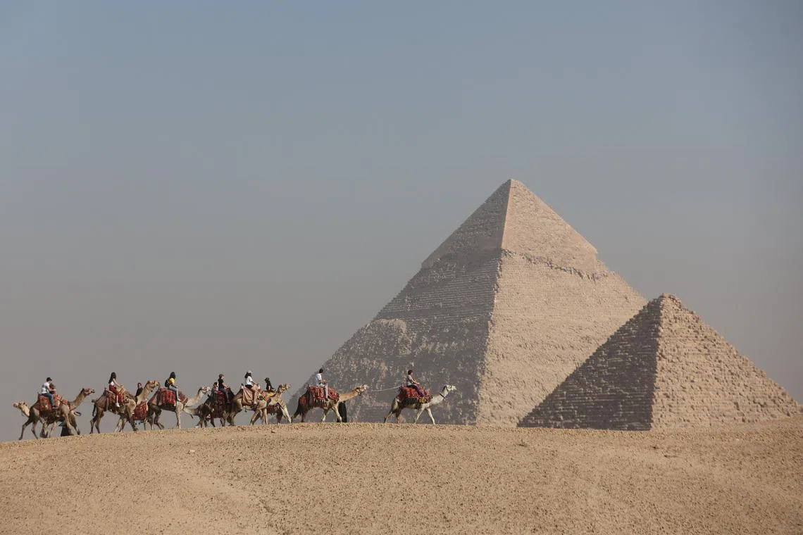 FILE PHOTO: Tourists ride camels in front of the Great Pyramids plateau in Giza, Egypt December 11, 2022. REUTERS/Amr Abdallah Dalsh/File Photo