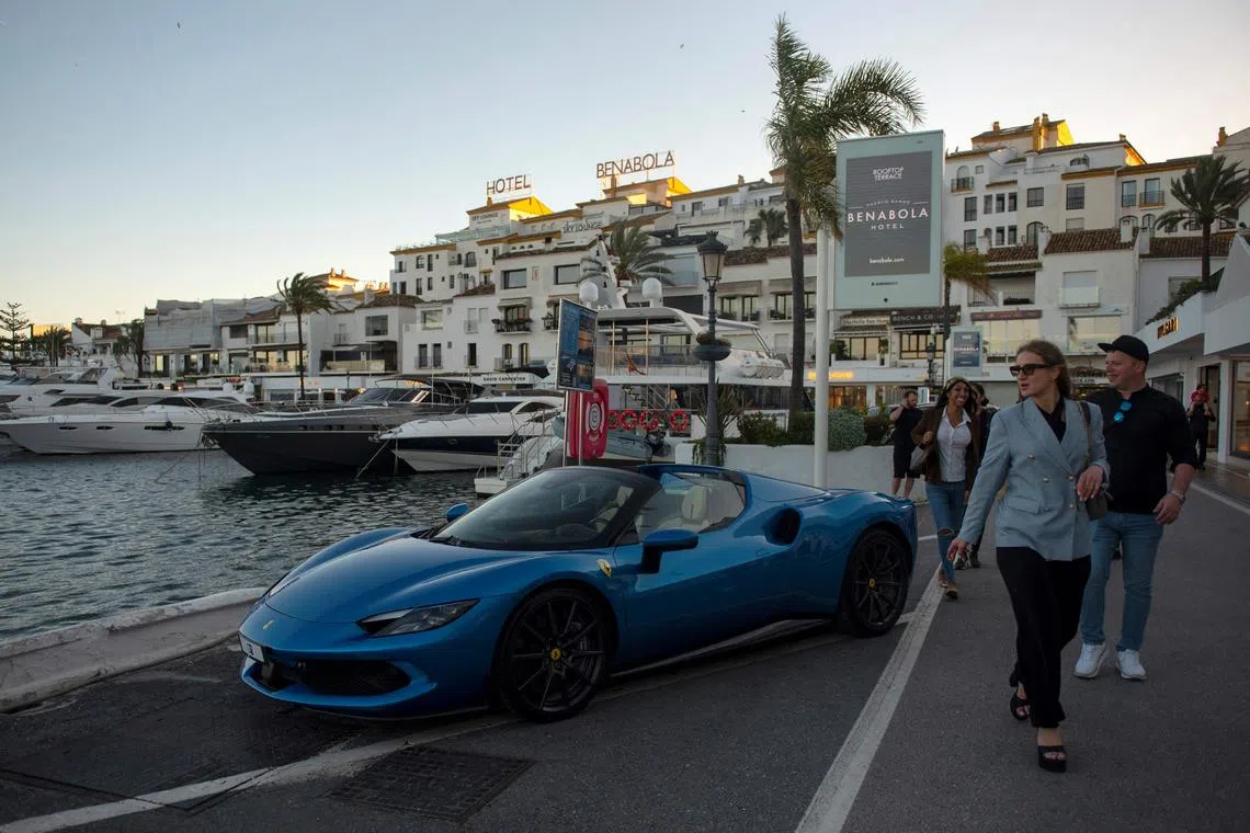 Pedestrians walk past a Ferrari in Puerto Banus luxury marina and shopping complex in Marbella on March 30, 2025. (Photo by JORGE GUERRERO / AFP)
