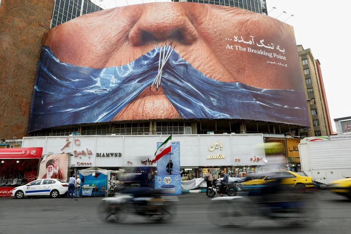 People drive past a billboard depicting US President Donald Trump and the Strait of Hormuz, in Tehran, Iran.