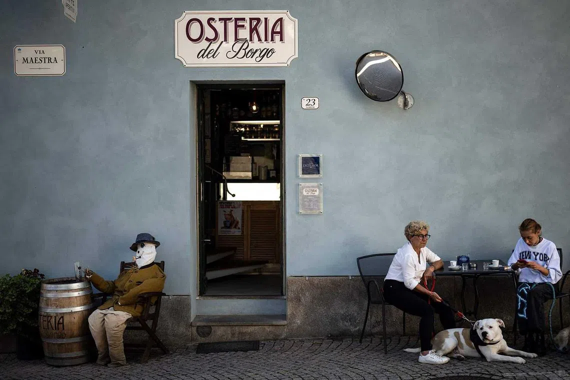 TOPSHOT - A picture taken on May 22, 2023 shows people having a coffee near a scarecrow displayed during the annual "Scarecrows Fair" in the Italian northern village of Castellar, near Cuneo. During the annual fair, people exhibit the scarecrow they made in gardens, courtyards, fields or streets. (Photo by Marco Bertorello / AFP)
