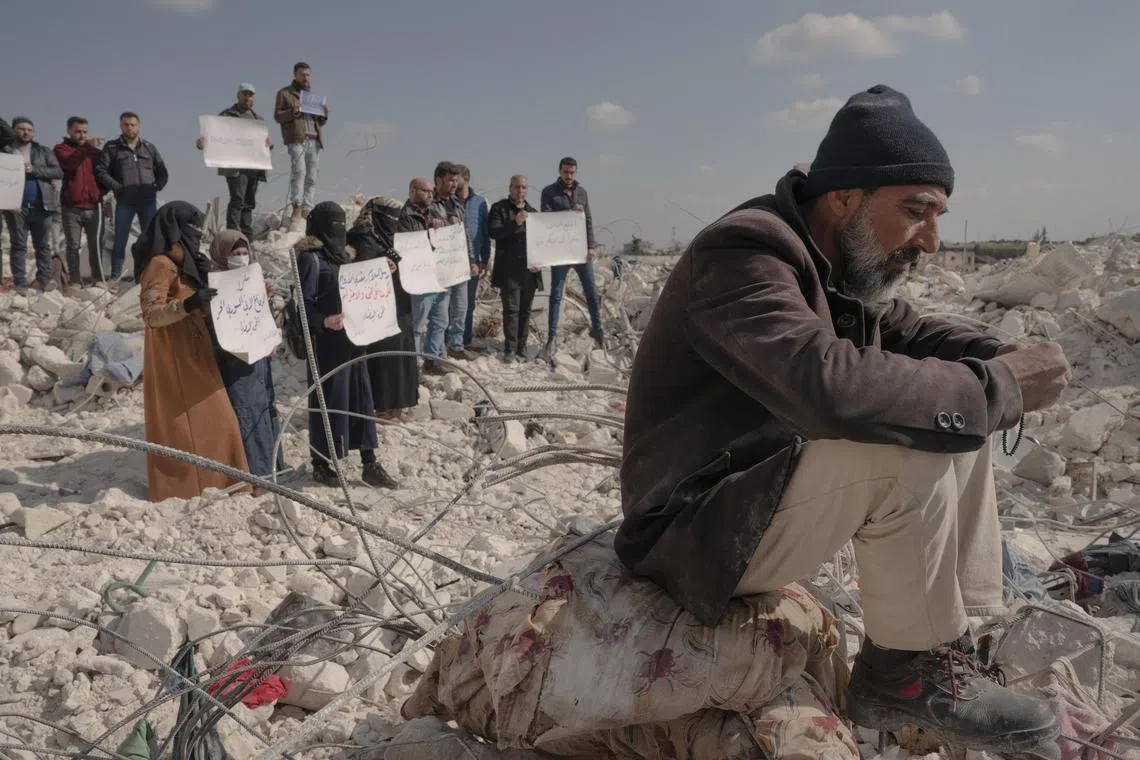 Syrians protest against lack of international aid, while a man sits on the rubble of his home in the Syrian town of al-Atarib.