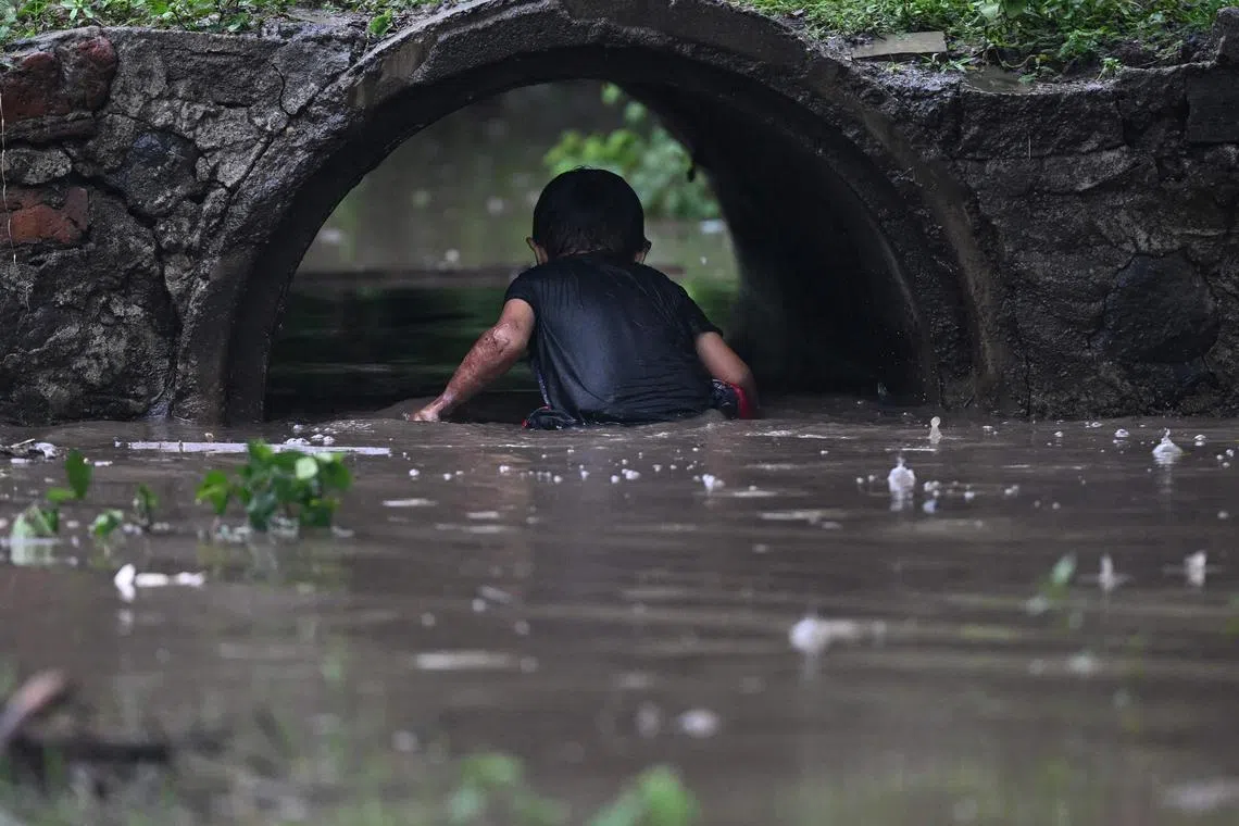 A boy plays in a pong during the red alert decreed by the government as Tropical Storm Pilar threatened to make landfall, in Jiquilisco, El Salvador, on October 31, 2023. Tropical storm Pilar scraped past Central America Tuesday, causing heavy rains along the Pacific coast but growing less likely to make landfall. With maximum sustained winds of 50 miles (80 kilometers) per hour, Pilar was slowly moving towards El Salvador, but its core "is expected to remain offshore," the US National Hurricane Center said in a statement. (Photo by Marvin RECINOS / AFP)