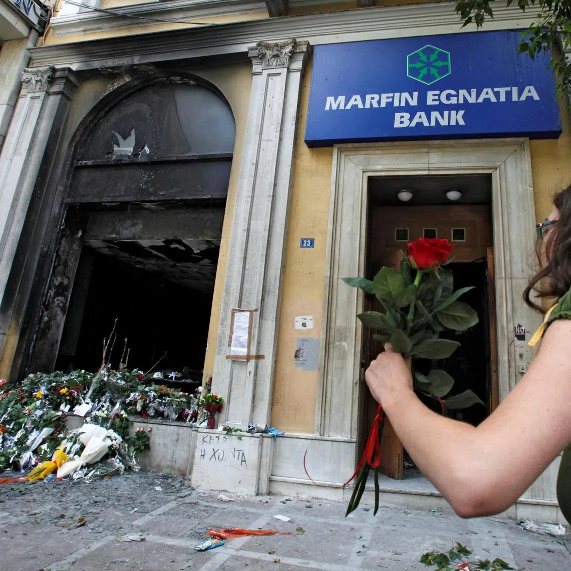 FILE PHOTO: A woman arrives to place a flower outside a burned-out bank, May 6, 2010 , which was set on fire during violent demonstrations in Athens a day earlier. REUTERS/Pascal Rossignol/File Photo