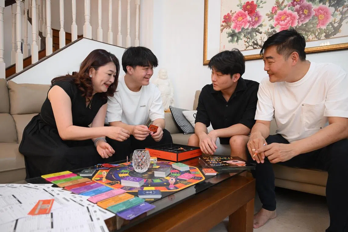 Ms Stella Hoh and Mr Daniel Ku (both far left and right) with their children Yu Heng (in white) Ee Waynne (in black) playing a financial education board game, Wealth and Joy Simulation, that the family uses to make learning about financial literacy fun.