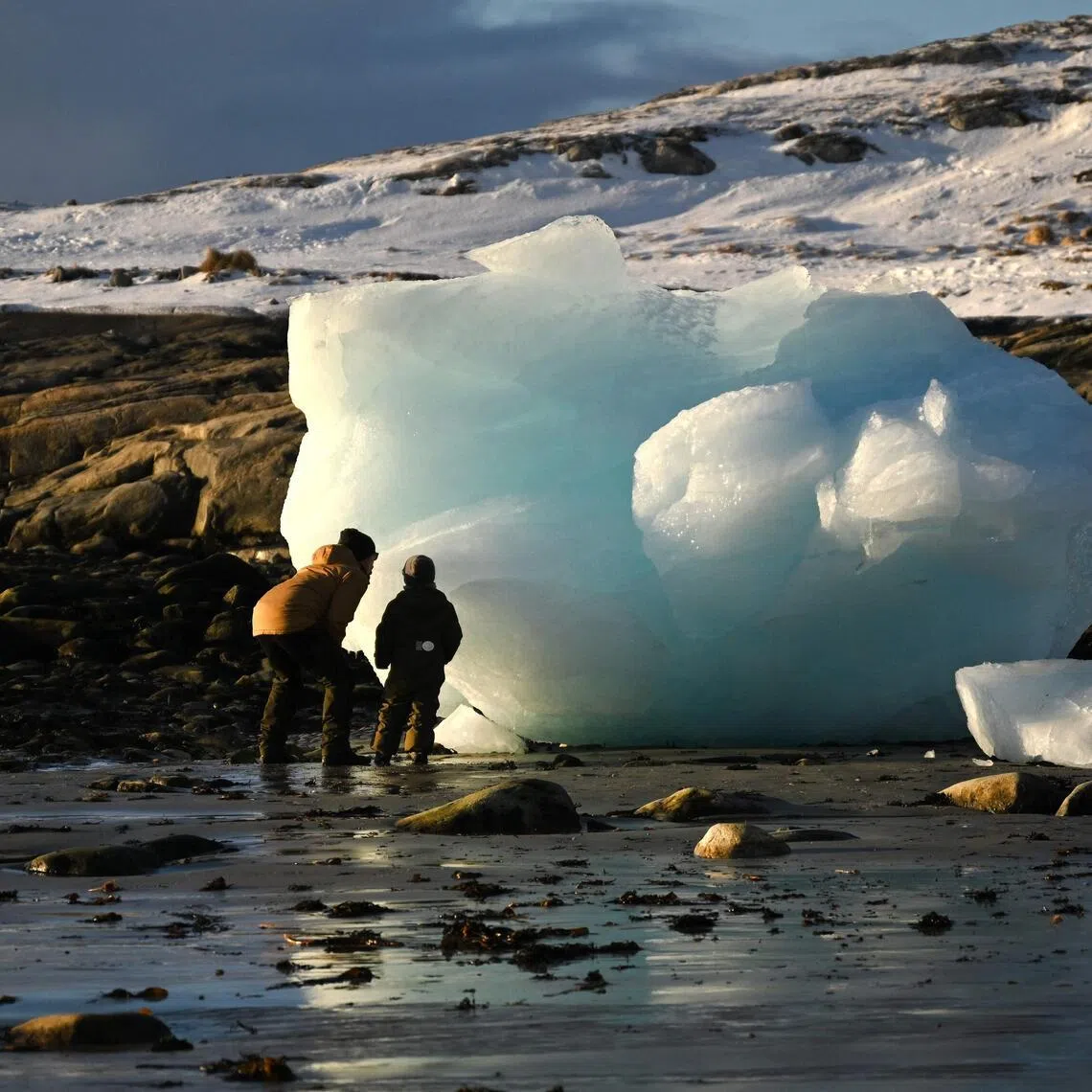 A father and his son look to an ice block at the coastline in the city of Nuuk, western Greenland, on February 4, 2026. (Photo by Ina FASSBENDER / AFP)