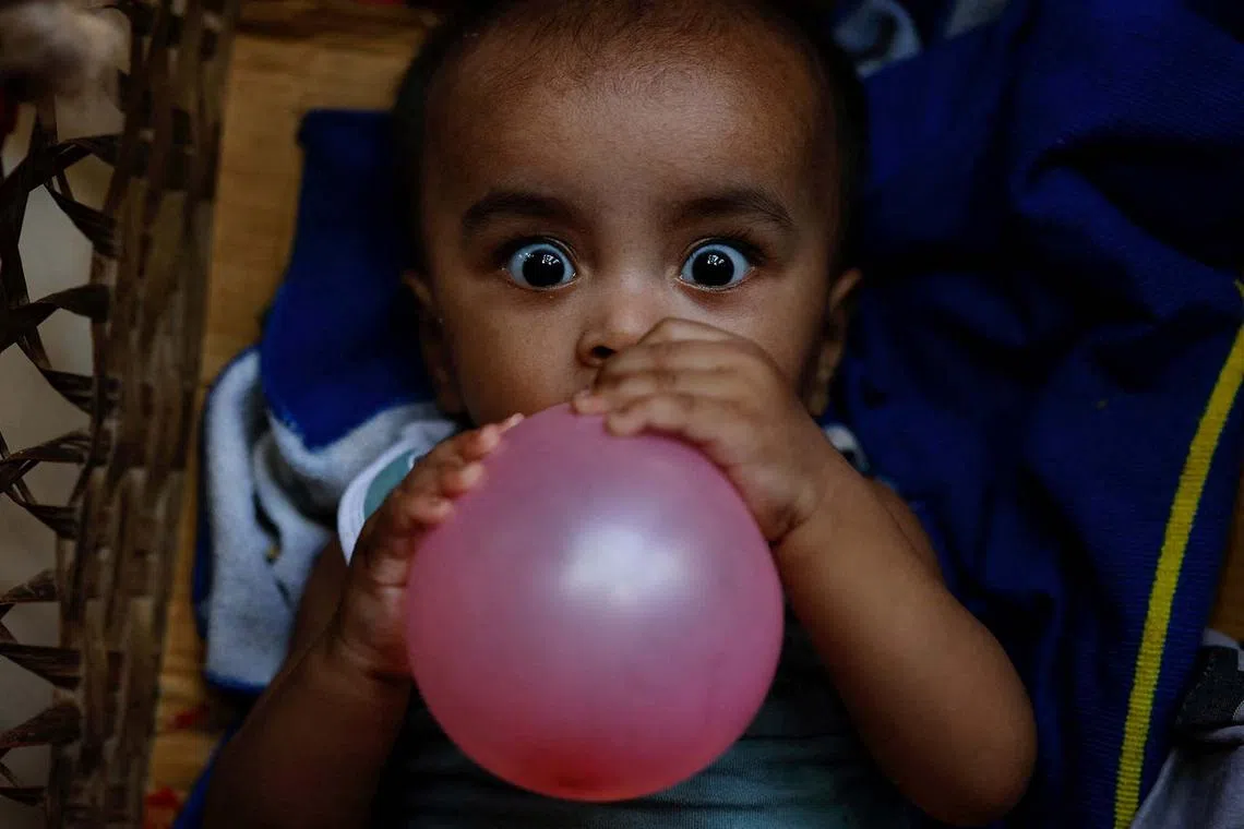 A Rohingya refugee child holding a balloon while lying on a cradle at a refugee camp in Cox's Bazar, Bangladesh, Aug 18, 2025. 